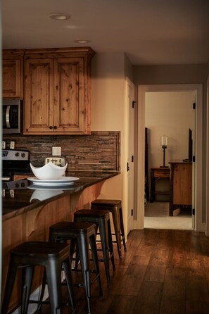 A kitchen with wooden cabinets, a stone backsplash, and a bar area with stools. - King of Mountain: Hot Tub, Grill, Games, Pet-Friendly! (Gatlinburg)