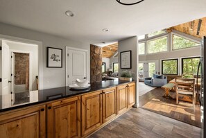 A modern kitchen with wooden cabinets, a black countertop, and a stone accent wall. - King of Mountain: Hot Tub, Grill, Games, Pet-Friendly! (Gatlinburg)