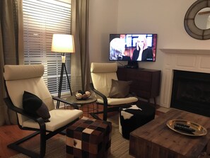 Ein Wohnzimmer mit zwei Sesseln, einem Couchtisch, einem Fernseher und einem Kamin.