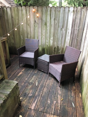 Eine Holzterrasse mit zwei Korbstühlen und einem kleinen Tisch, umgeben von einem Holzzaun.