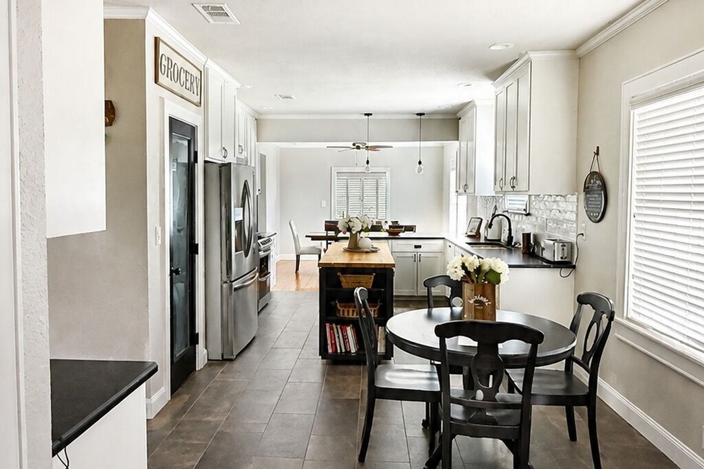 Una cocina moderna con armarios blancos, un comedor con una mesa y sillas redondas, y una isla central con un jarrón de flores.