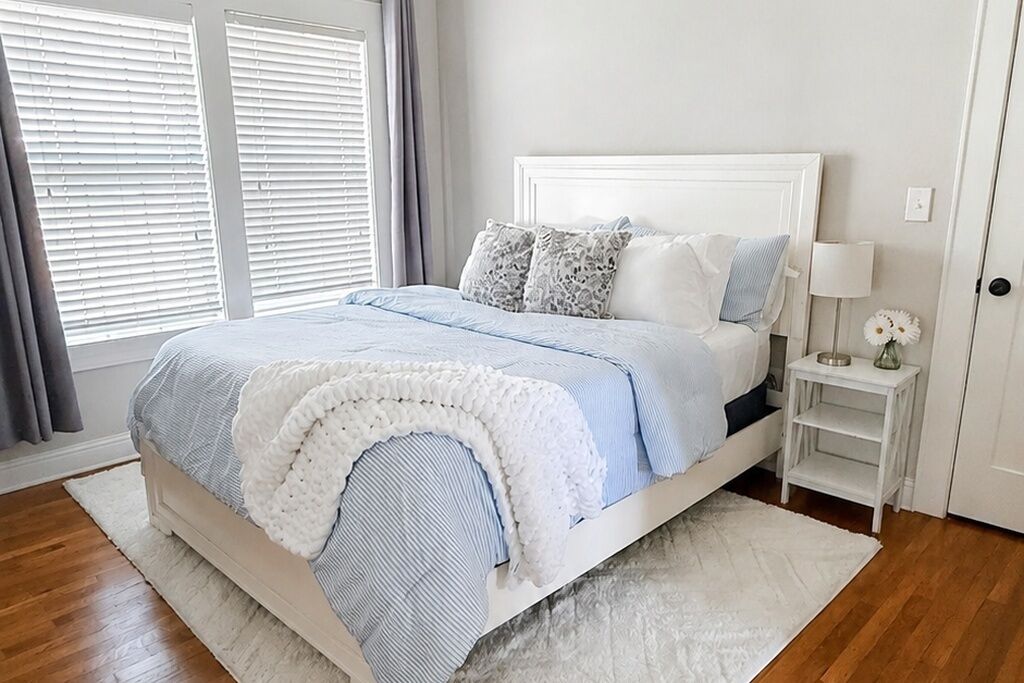 Une chambre à coucher avec un lit, une table de chevet, une lampe et une fenêtre avec des stores.