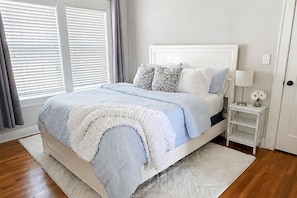 A bedroom with a bed, a nightstand, a lamp, and a window with blinds.