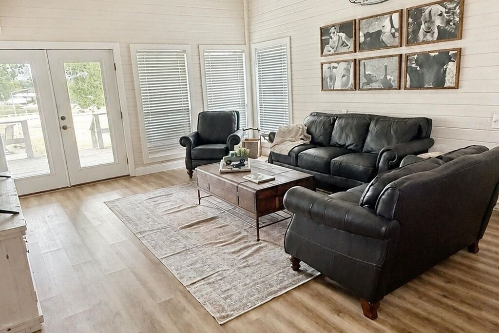 Un salon avec un canapé en cuir foncé, une table basse en bois et un tapis à motifs. On y trouve deux fauteuils, une cheminée et un ensemble de tableaux encadrés accrochés au mur.