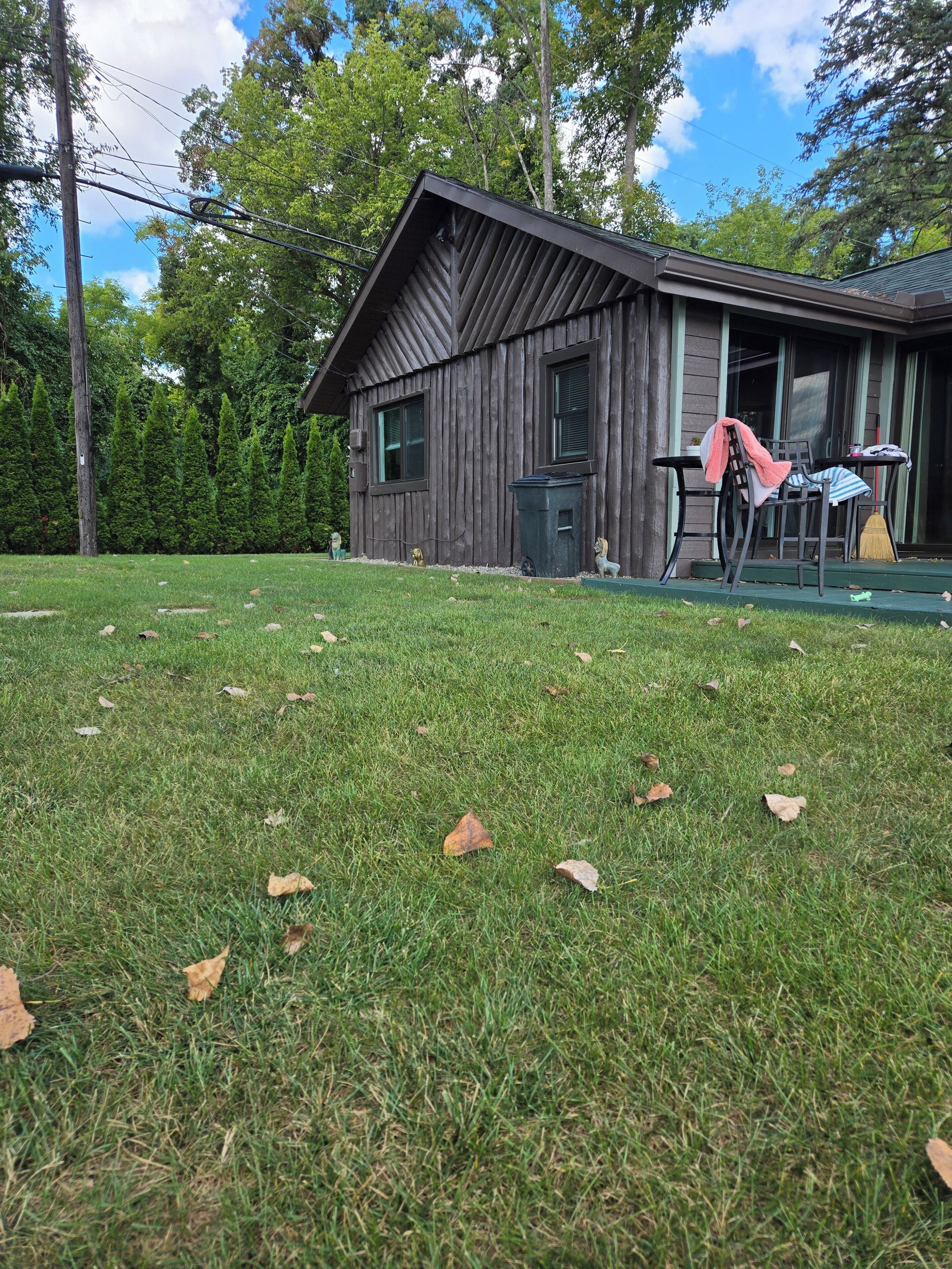 A wooden cabin with a porch, a green lawn, and a clear sky.