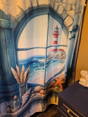 A room with a large window featuring a mural of a lighthouse, ocean waves, and seashells.