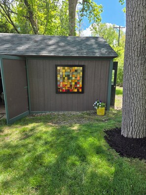 A small shed with a colorful mosaic window, surrounded by grass and trees.