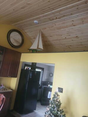 A kitchen with wooden ceiling, a refrigerator, a clock, and a small Christmas tree.