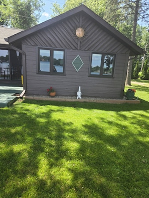 A small wooden cabin with a sloped roof, a front porch, and a window overlooking a body of water.