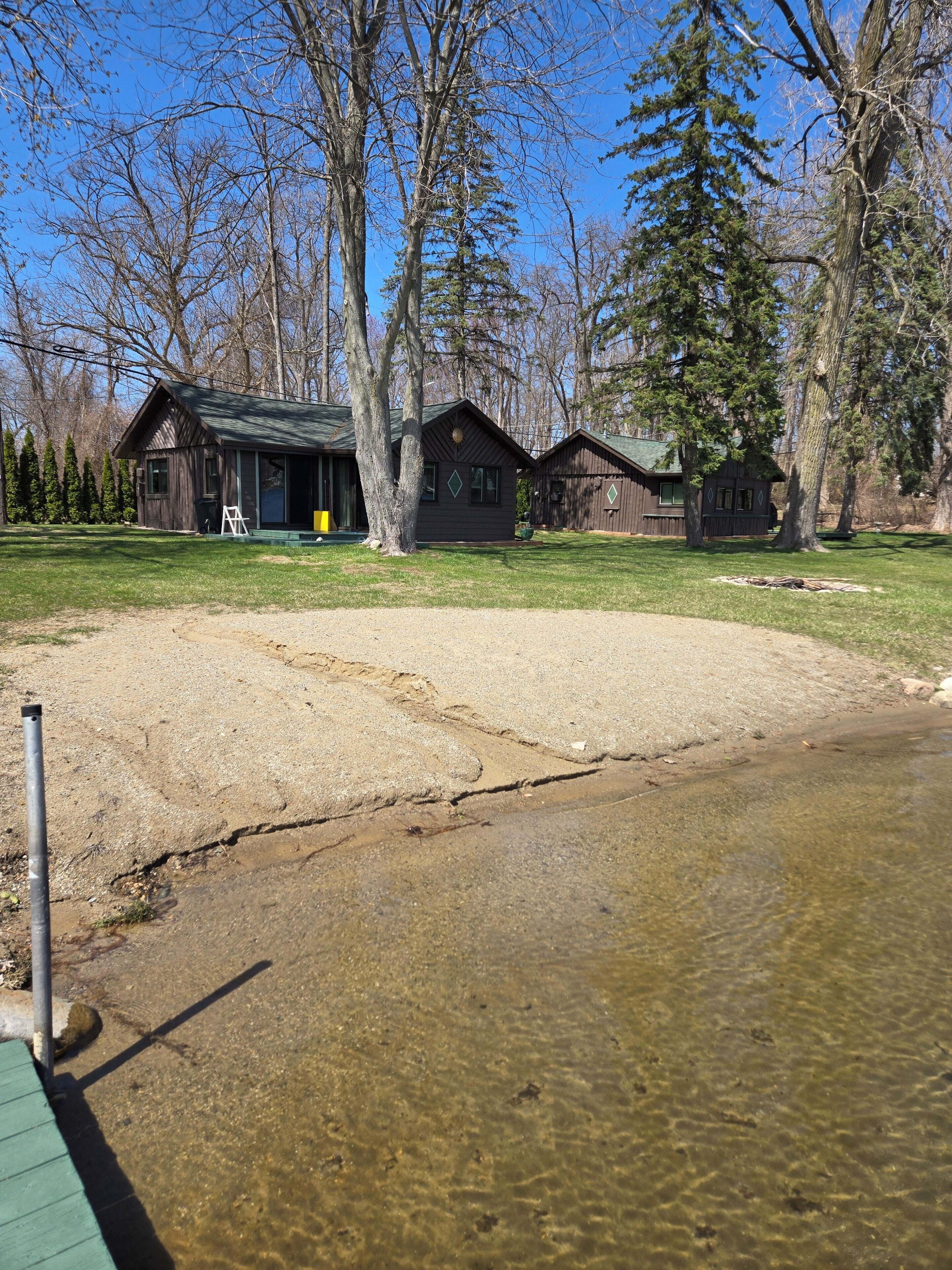 A cabin with a deck, a sandy area, and a clear water body.