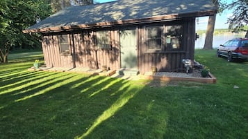 A small wooden cabin with a sloped roof, surrounded by a well-maintained lawn and trees.