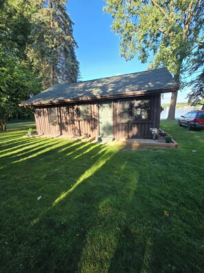 A small wooden cabin with a sloped roof, surrounded by a well-maintained lawn and trees. - Cozy 1-bedroom cabin in amazing White Lake with AC on ALL SPORTS SUGDEN LAKE (White Lake)