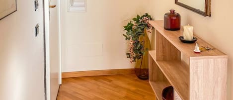 A hallway with wooden flooring, a white door, a wooden console table with decorative items, and wall-mounted artwork.