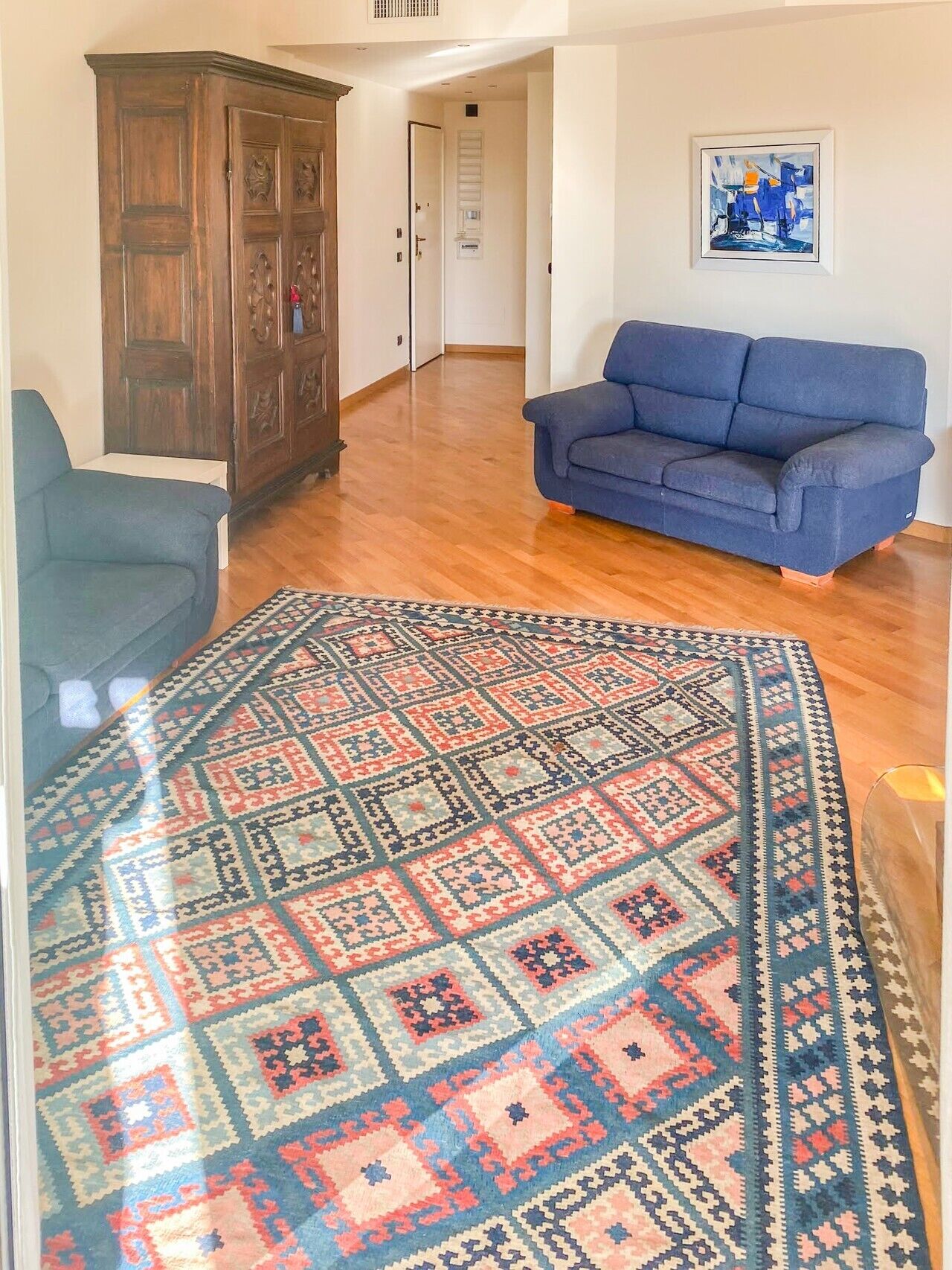 Un salon avec un canapé bleu, un tapis à motifs, un meuble en bois et une porte donnant sur une autre pièce.