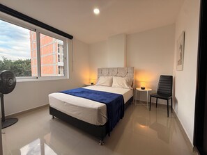 A modern bedroom with a large bed, two bedside lamps, a chair, and a standing fan. - Beautiful 4 bedroom apartment in Medellín perfect for your stay (Medellín)