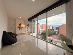 A modern living room with a large window, a black bean bag, a white chair, and a floor lamp. - Beautiful 4 bedroom apartment in Medellín perfect for your stay (Medellín)