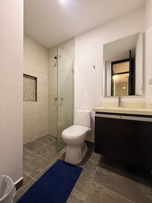 A modern bathroom with a glass shower enclosure, a white toilet, a dark-colored vanity, and a blue bath mat. - Beautiful 4 bedroom apartment in Medellín perfect for your stay (Medellín)