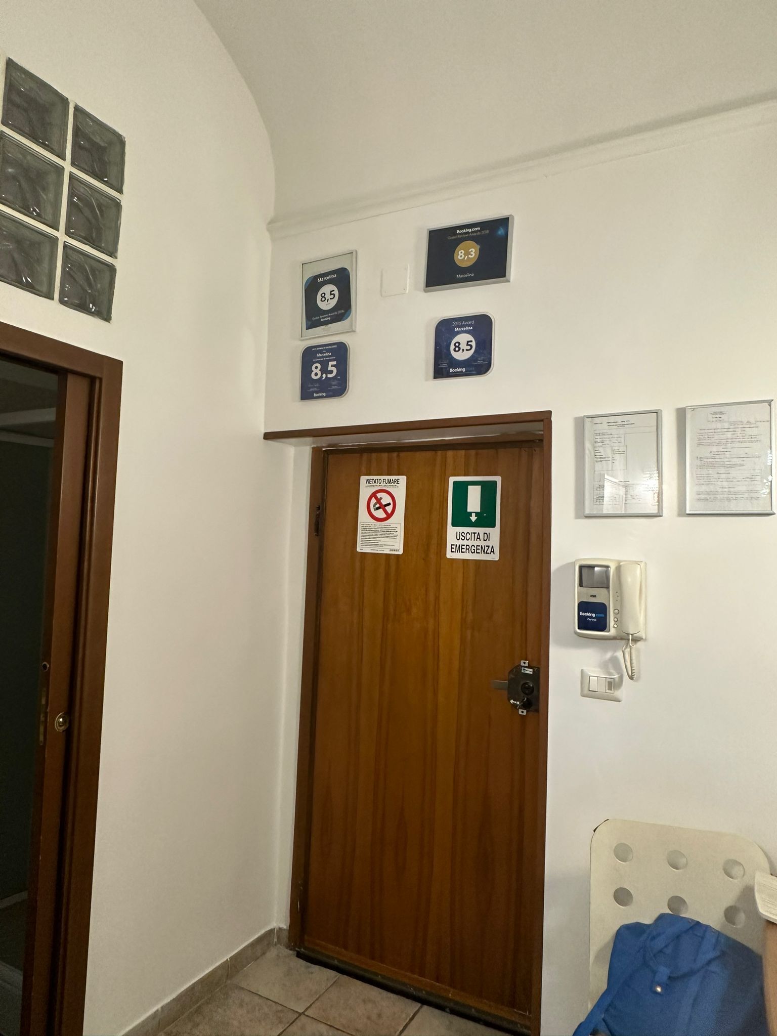 Habitació d'hotel amb una porta de fusta, un cartell de prohibició de fumar, un senyal d'eixida d'emergència i una màquina de reserves.