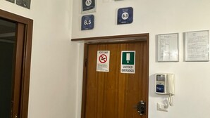 A hotel room with a wooden door, a no-smoking sign, emergency exit sign, and a booking machine.