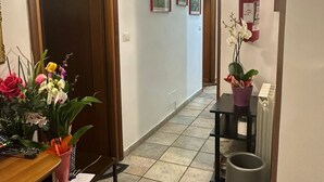 A hallway with a wooden door, a tiled floor, a small table with a vase of flowers, and a trash can.