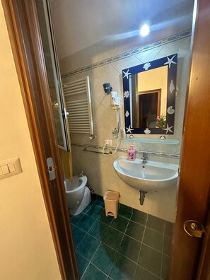 Et badeværelse med en hvid vask, et spejl med dekorative detaljer, en bidet og en skraldespand.