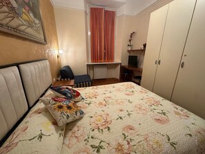 Et soveværelse med seng, skrivebord, stol og skab.