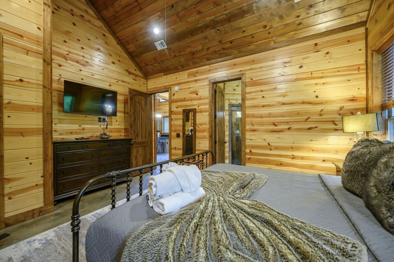 Een kamer met houten lambrisering, een bed, een dressoir, een televisietoestel en een lamp.