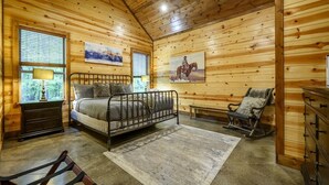 Camera da letto in una baita di legno, con un letto, una poltrona a dondolo, una panca e un comò.