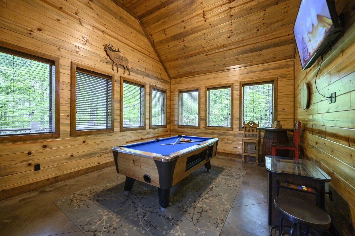 A wooden interior with a pool table, windows, and a television.