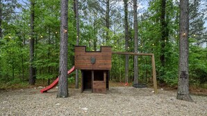 Una casetta di legno con uno scivolo e un'altalena in una zona boschiva.