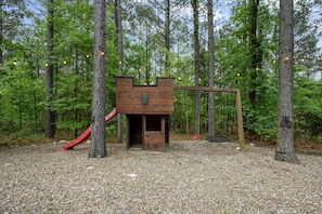 Une cabane en bois avec un toboggan et une balançoire, située dans une zone boisée.