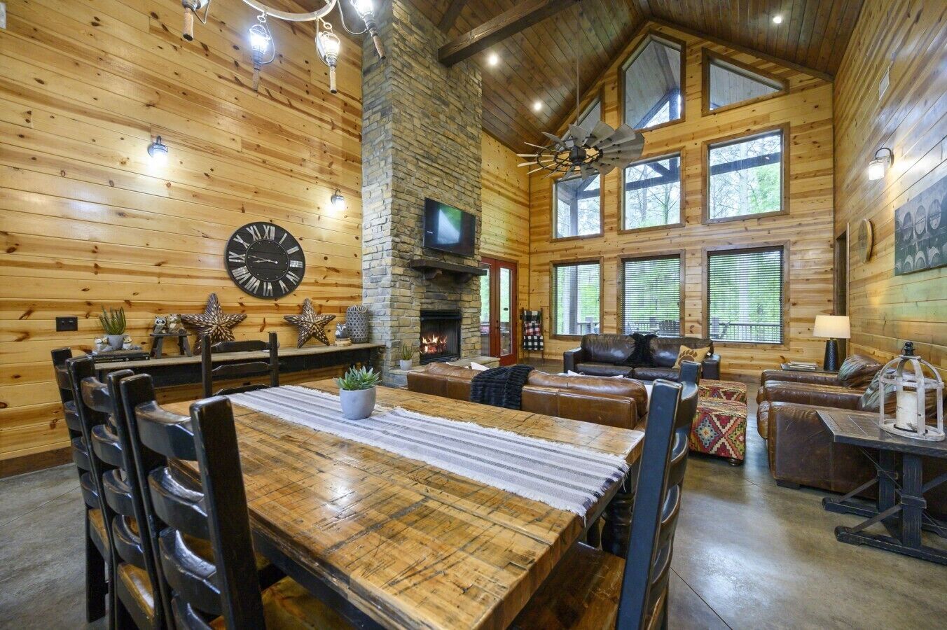 A log cabin interior with a dining area, fireplace, leather seating, and large windows.