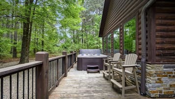 Eine Holzterrasse mit Whirlpool und Stühlen, umgeben von Bäumen.