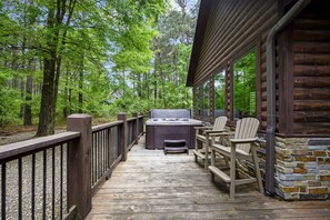A wooden deck with a hot tub and chairs, surrounded by trees.