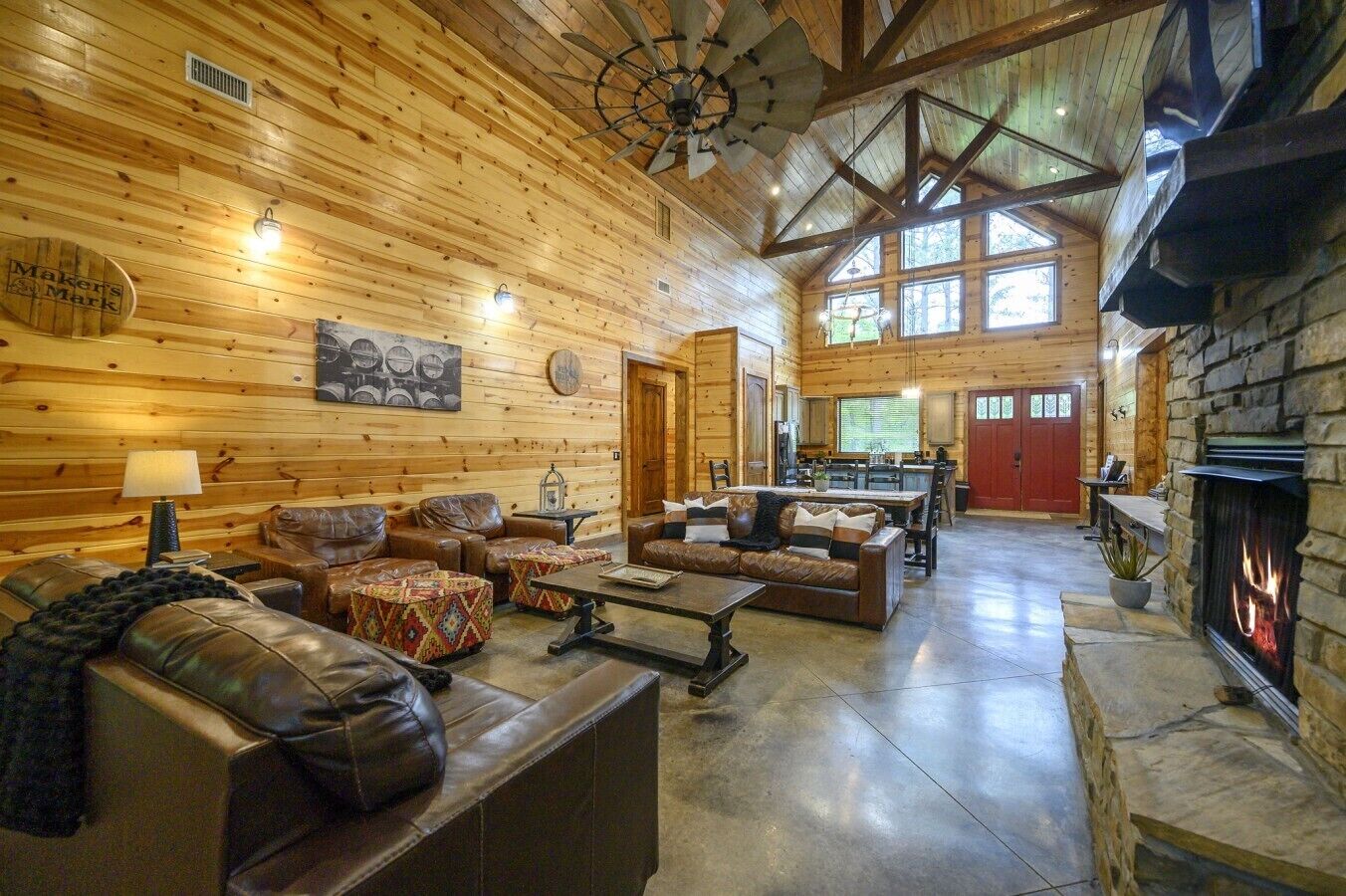 A log cabin interior with a fireplace, leather sofas, a dining area, and a large wooden ceiling.