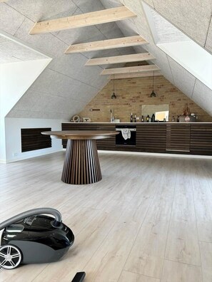 Ein geräumiger Loft mit hoher Decke, freiliegenden Holzbalken, einer Küche mit dunklen Schränken und einem runden Esstisch in der Mitte.