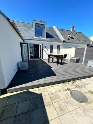 Ein Wohnhaus mit geneigtem Dach, einer Terrasse, einem Tisch und Stühlen sowie einem kleinen Außenbereich.