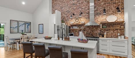 Une cuisine moderne avec un mur en briques, des appareils électroménagers en acier inoxydable et un îlot central doté de tabourets de bar.