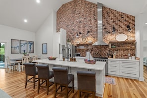 A modern kitchen with a brick wall, stainless steel appliances, and a central island with bar stools. - Lakefront MASTERS WEEK Rental (McCormick)