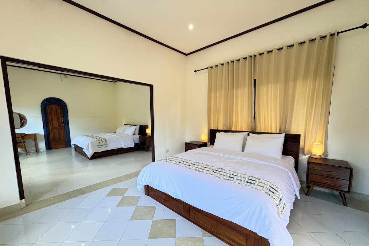 A bedroom with a large bed, a bedside table, a nightstand, a mirror, and a door.