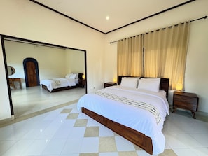 A bedroom with a large bed, a bedside table, a nightstand, a mirror, and a door. - Dhanda Homestay (Ubud)