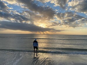 A person standing on a beach with the ocean and a cloudy sky in the background.