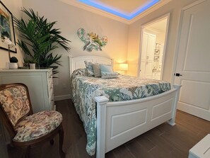 Een slaapkamer met een bed, een stoel, een kaptafel en een deur.