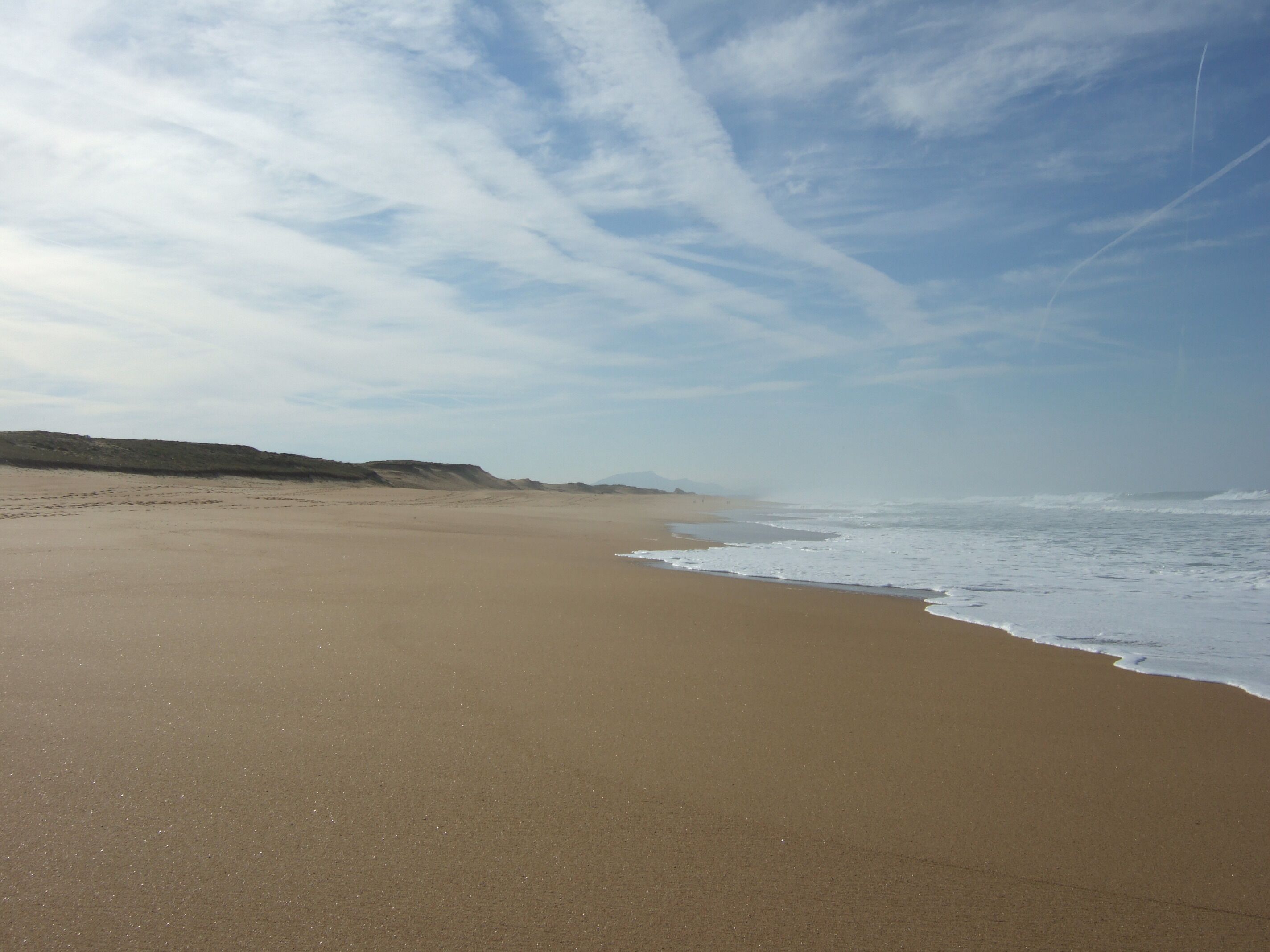 A wide sandy beach with gentle waves and a clear sky.