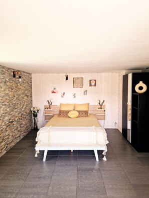 A bedroom with a large bed, a stone wall, and a wooden door. - Villa océan-Achard-Labenne, near the dune.Pool/Spa /Sleeps 8/10 and pets welcome (Labenne)