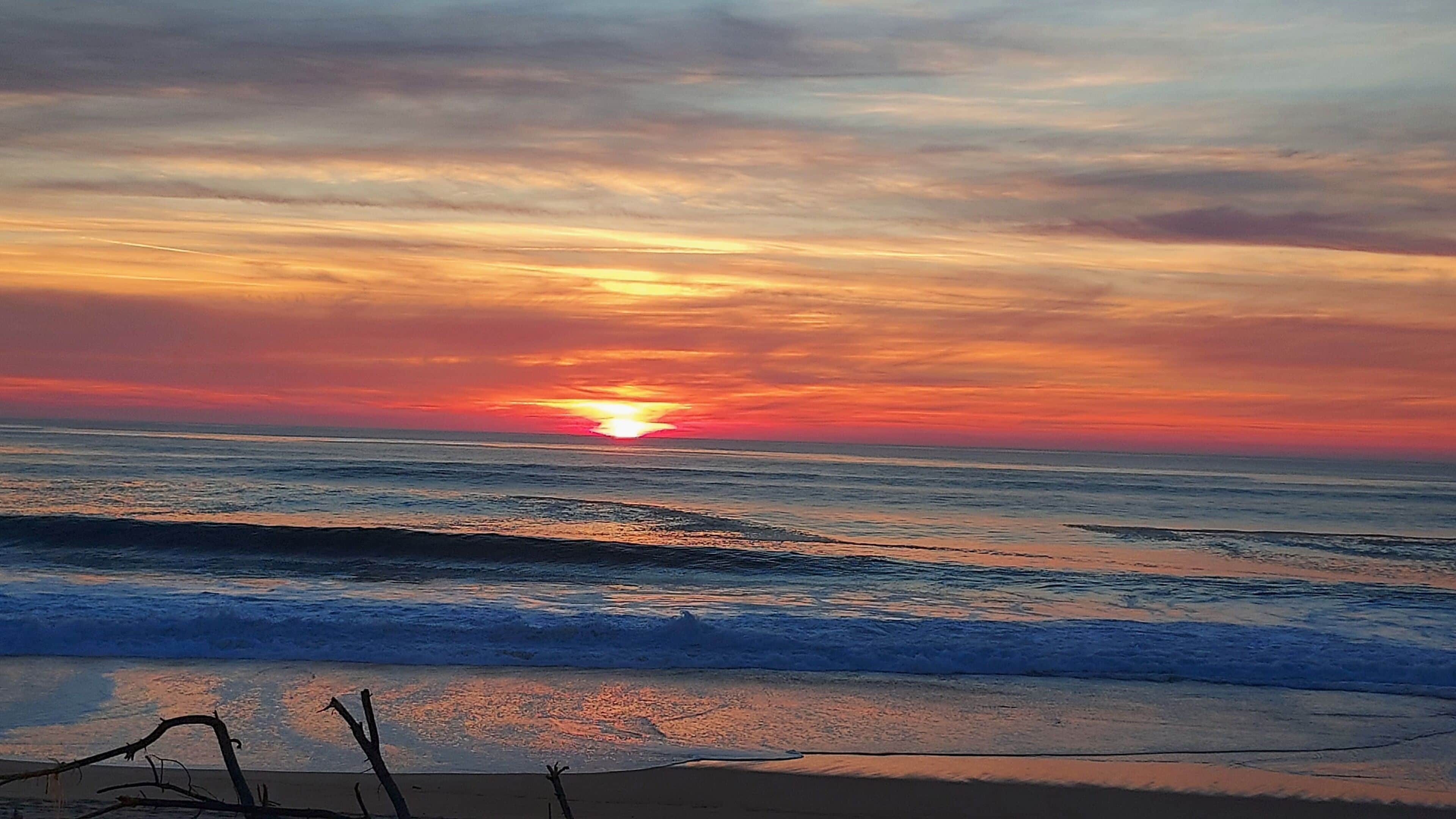 Um pôr do sol sobre o oceano, com ondas se aproximando da praia.