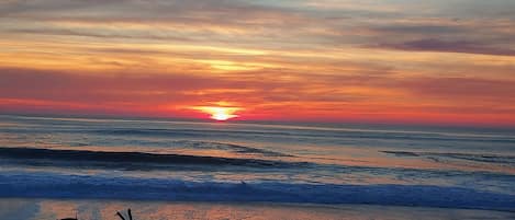 Um pôr do sol sobre o oceano, com ondas se aproximando da praia.