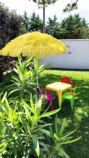A small outdoor seating area with a table and chairs, surrounded by green plants and a yellow umbrella. - Villa océan-Achard-Labenne, near the dune.Pool/Spa /Sleeps 8/10 and pets welcome (Labenne)
