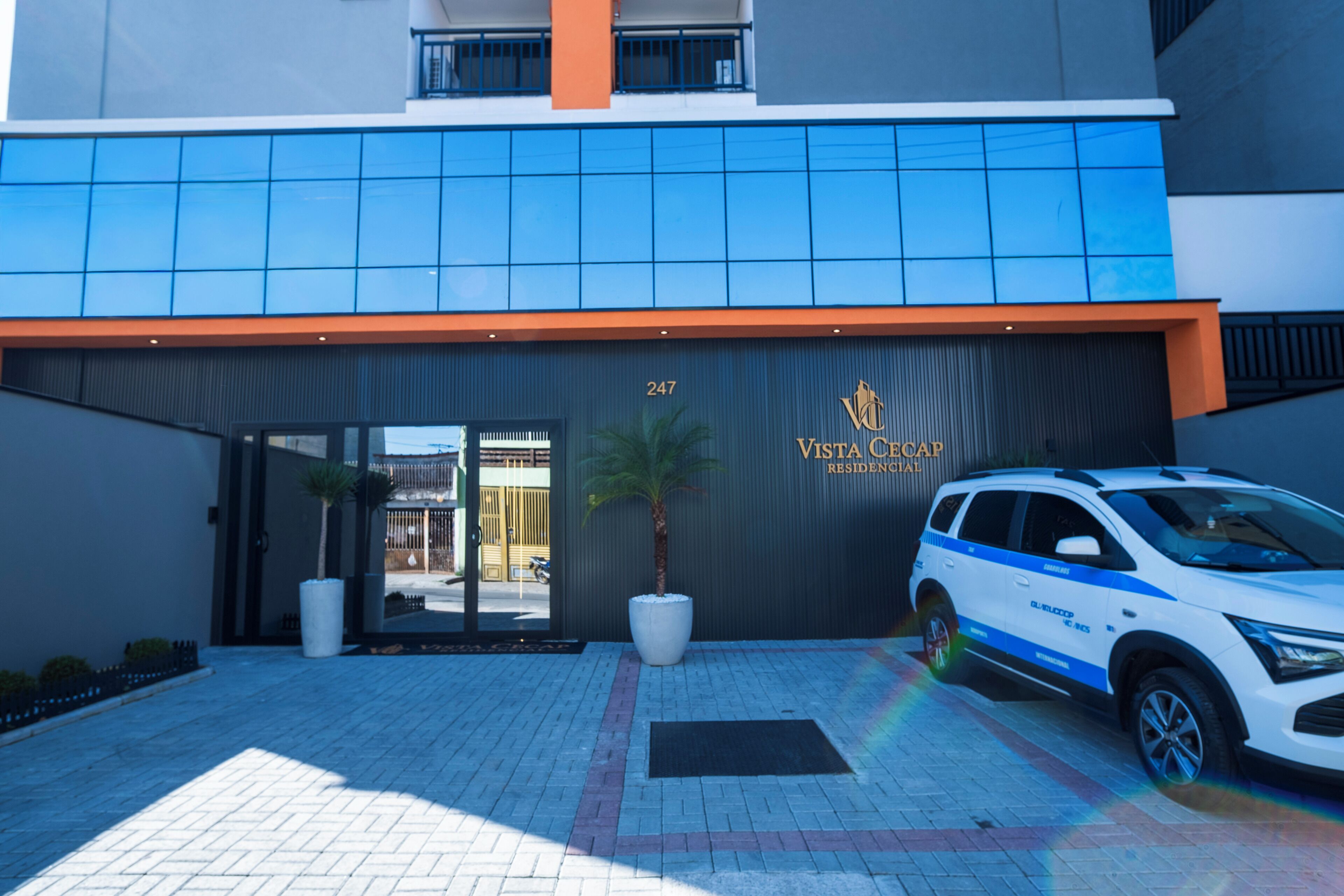 A modern building with a blue-tiled entrance, a numbered address sign, and a parked vehicle.