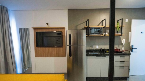 Habitación de hotel pequeña con cama, kitchenette, refrigerador, microondas y un rincón de comedor.